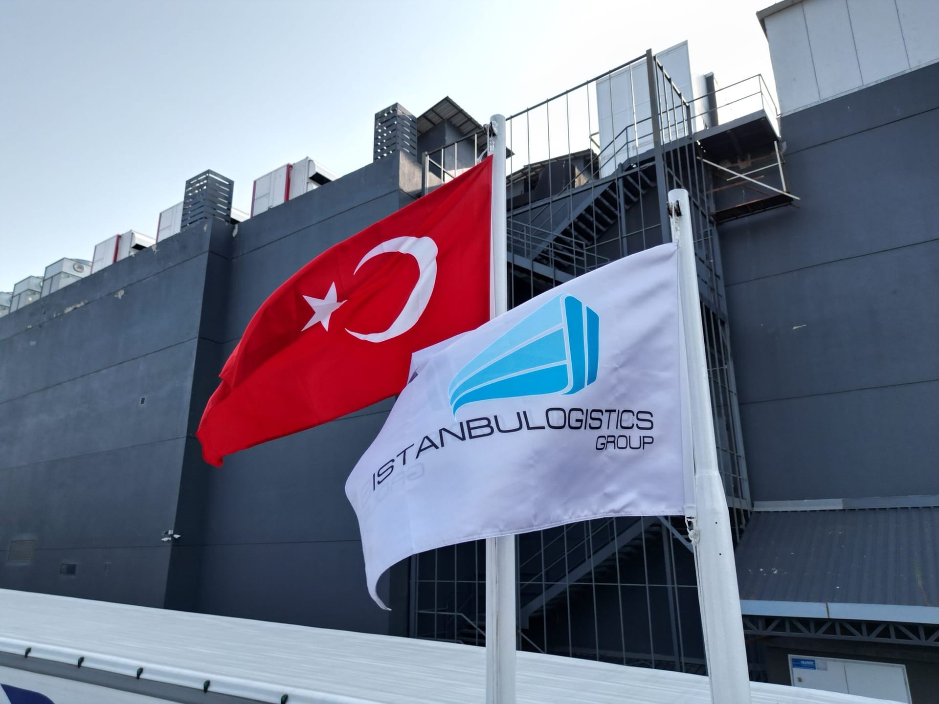Tesis önünde dalgalanan Türk bayrağı ve Istanbul Logistics Group bayrağı